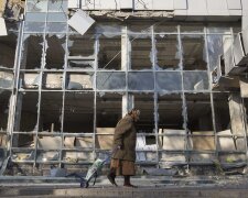 A woman pulls her shopping trolley as she walks past a building that was damaged by shelling in Done