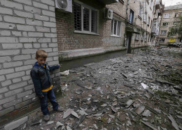 A boy plays near a residential building, damaged by what locals say was overnight shelling by Ukrain