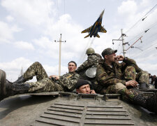 A fighter jet flies above as Ukrainian soldiers sit on an armoured personnel carrier in Kramatorsk