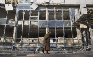 A woman pulls her shopping trolley as she walks past a building that was damaged by shelling in Done