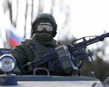 A military personnel member, believed to be a Russian serviceman, stands guard on a military vehicle