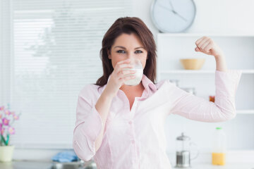 Portrait of young woman drinking milk and flexing muscles in the kitchen