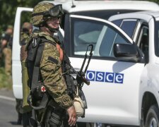 An armed pro-Russian separatist looks next to an OSCE monitoring mission in Ukraine vehicle, on the 