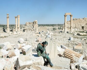 SYRIA. Palmyra / Tadmor. 1 April 2016. A Syrian Army soldier removes his helmet, sitting on the rubble of the former Temple of Bel, one of several sites in Ancient Palmyra destroyed by Islamic State militants.