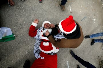 A man tends to a Palestinian protester, dressed as Santa Claus, after inhaling tear gas fired by Israeli troops during clashes in the West Bank city of Bethlehem, December 23, 2016. REUTERS/Mussa Qawasma