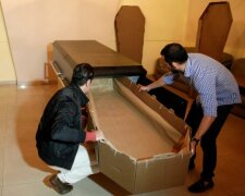Elio Angulo and Alejandro Blanchard put a cardboard coffin inside a crate at a mortuary in Valencia