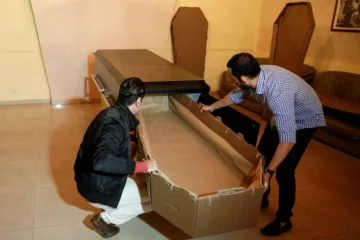 Elio Angulo and Alejandro Blanchard put a cardboard coffin inside a crate at a mortuary in Valencia