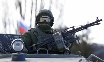 A military personnel member, believed to be a Russian serviceman, stands guard on a military vehicle