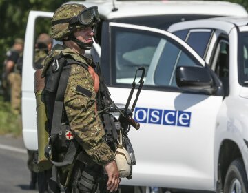 An armed pro-Russian separatist looks next to an OSCE monitoring mission in Ukraine vehicle, on the 