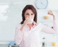 Portrait of young woman drinking milk and flexing muscles in the kitchen